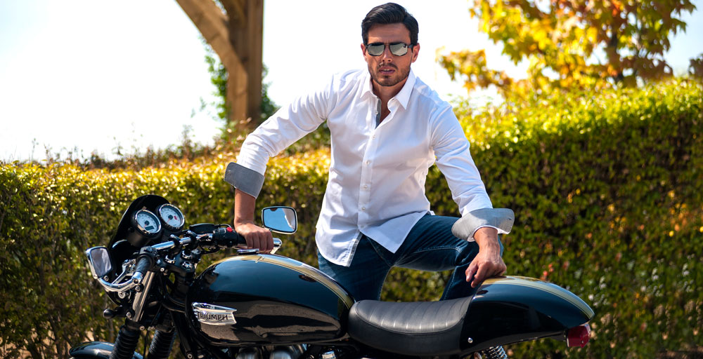 homme en chemise qui pose à côté d'une moto